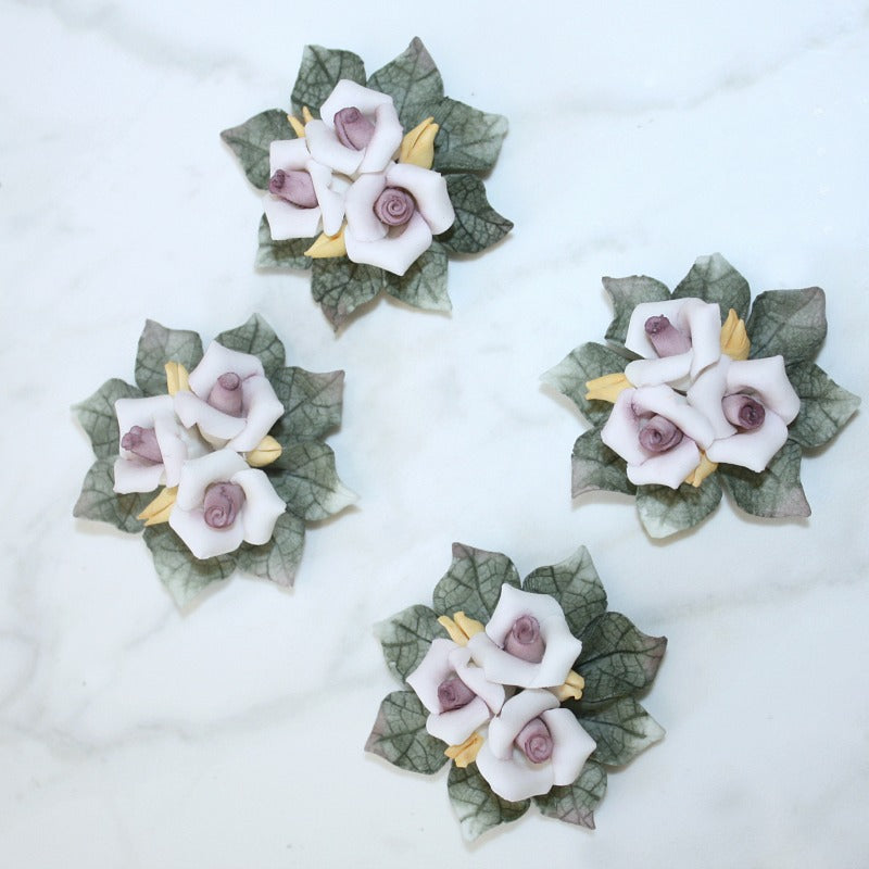 A set of four small, handmade porcelain bouquets with pink and mauve flowers, presented on a marble surface.