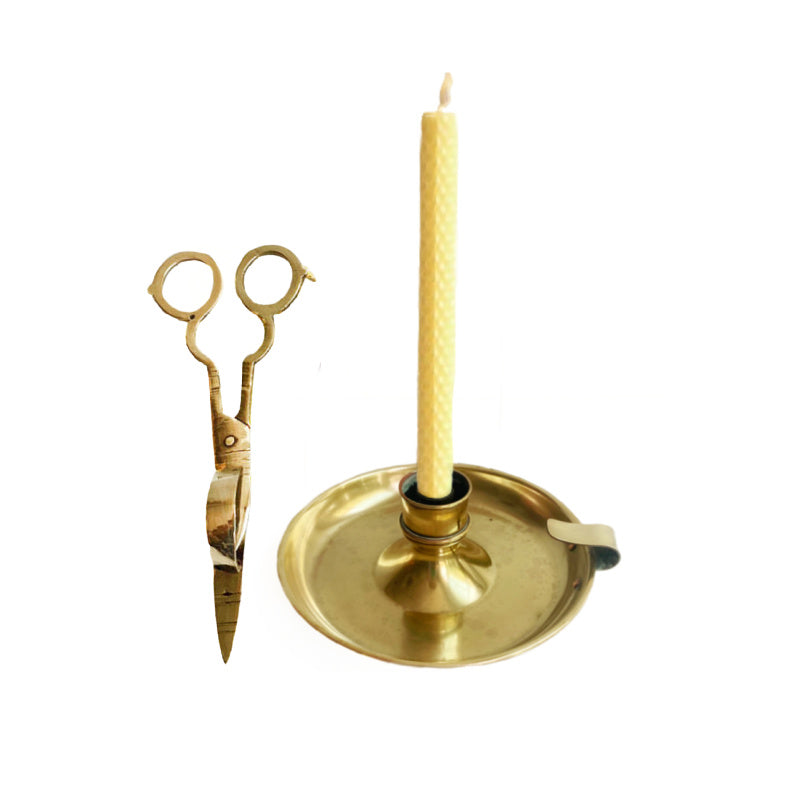Antique brass chamberstick candle holder with a wick trimmer, featuring a wide lower dish, a holding ring with copper bolts, and a pair of scissors standing next to it.