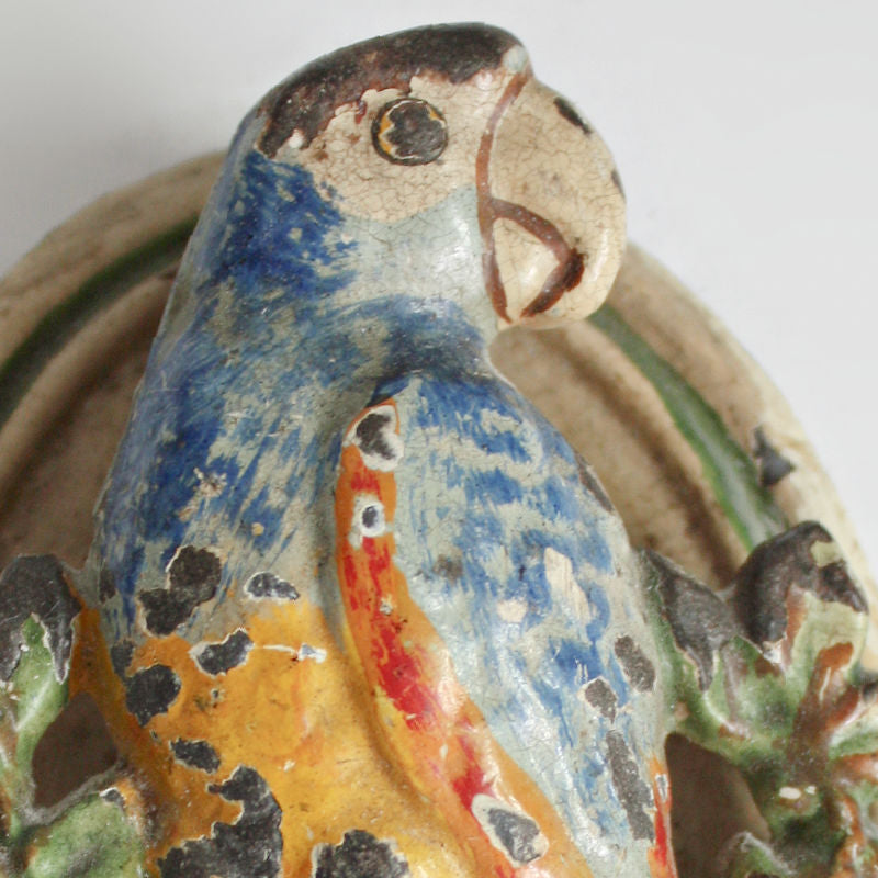 Antique cast iron door knocker shaped like a parrot with bright multicolored paint, showing signs of wear and aging.