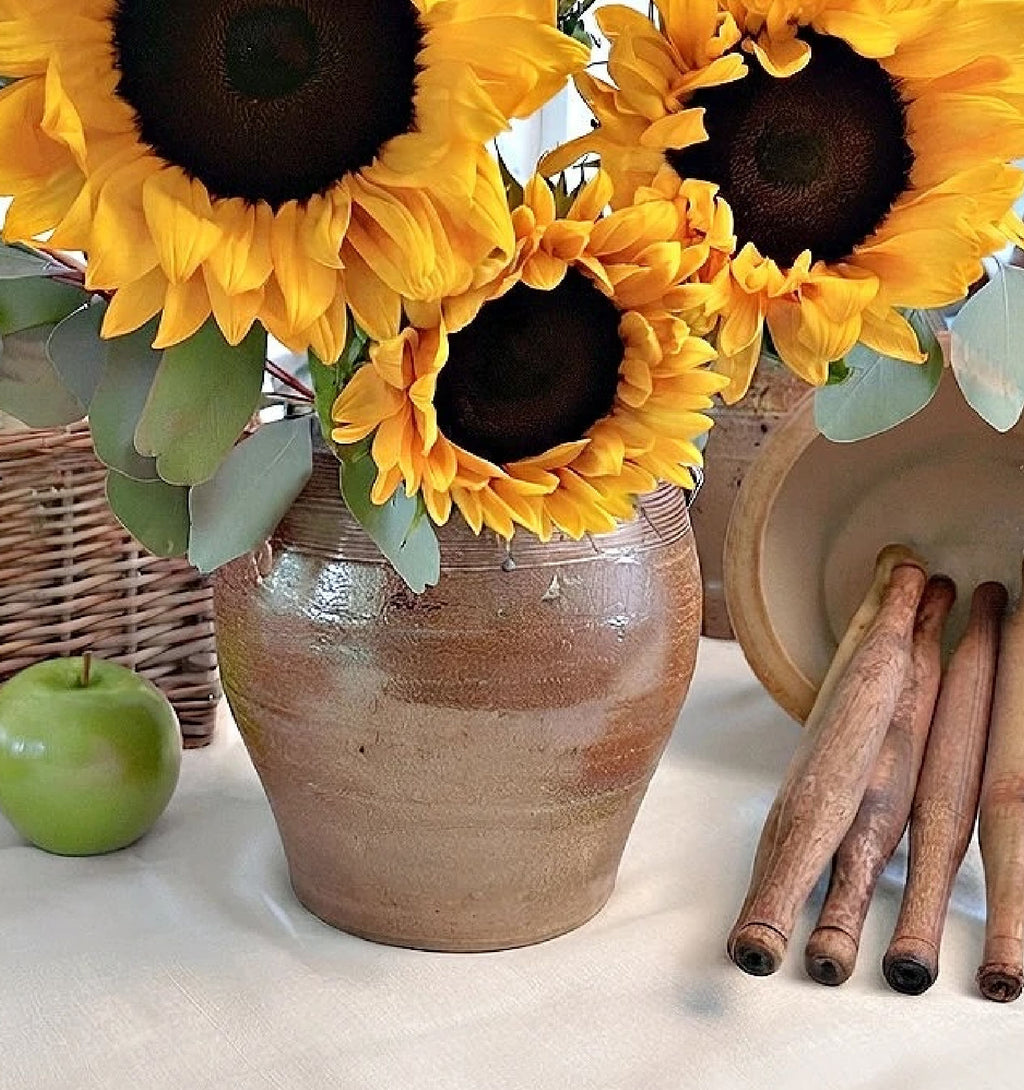 antique French confit pot with lug handles holding sunflowers on a table set with linen
