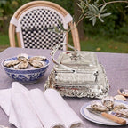Decorative antique silver English Sardine box on a table with oysters and a checkered chair in the background