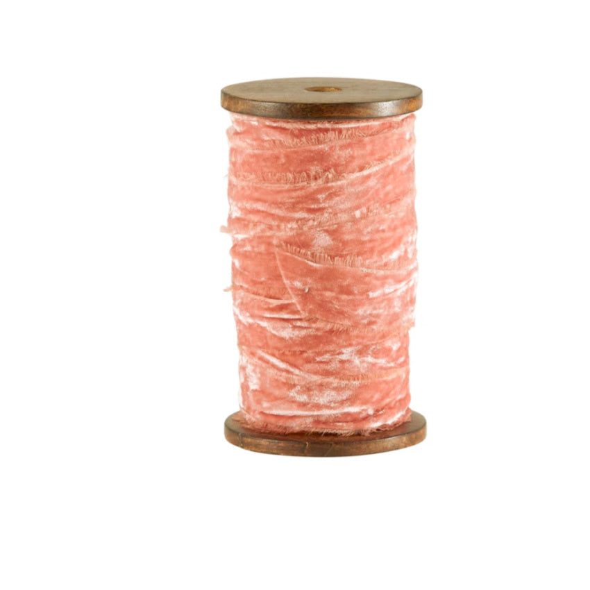 A spool of apricot rose colored velvet ribbon with frayed edges.