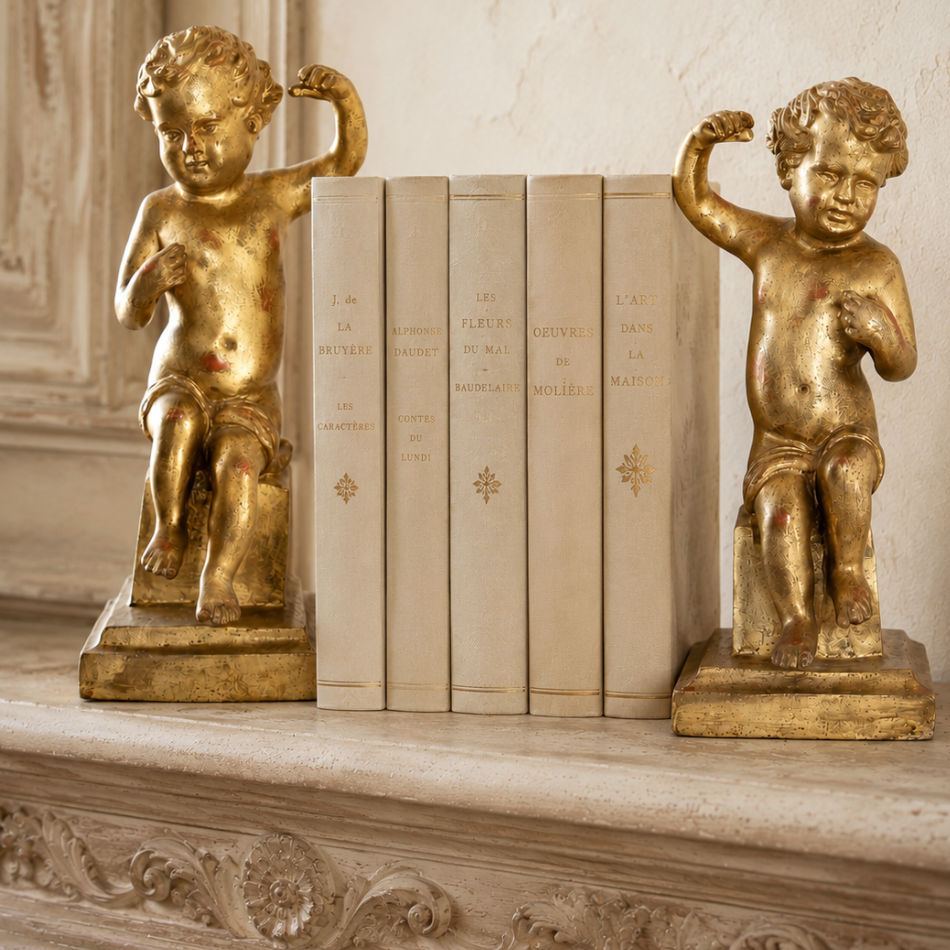 Antique Baroque giltwood putti sculptures on pedestal bases with antique cream books on an antique French COntry mantel