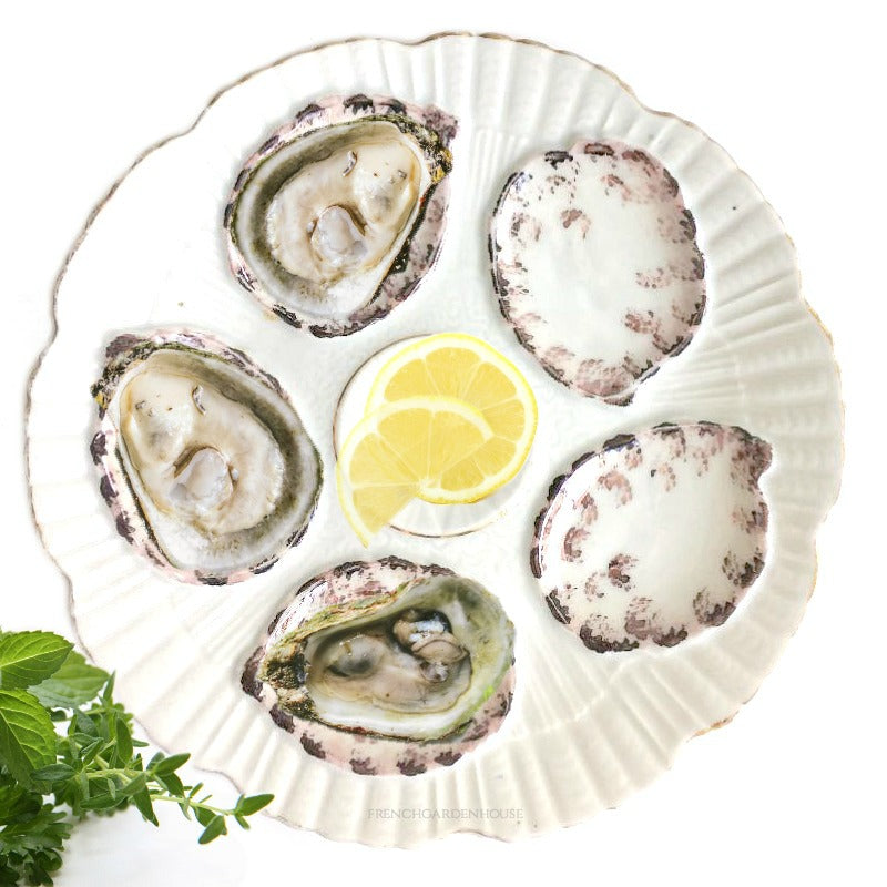 An antique porcelain oyster plate with purple luster details, featuring five wells for oysters and a central spiral well for lemon or butter.