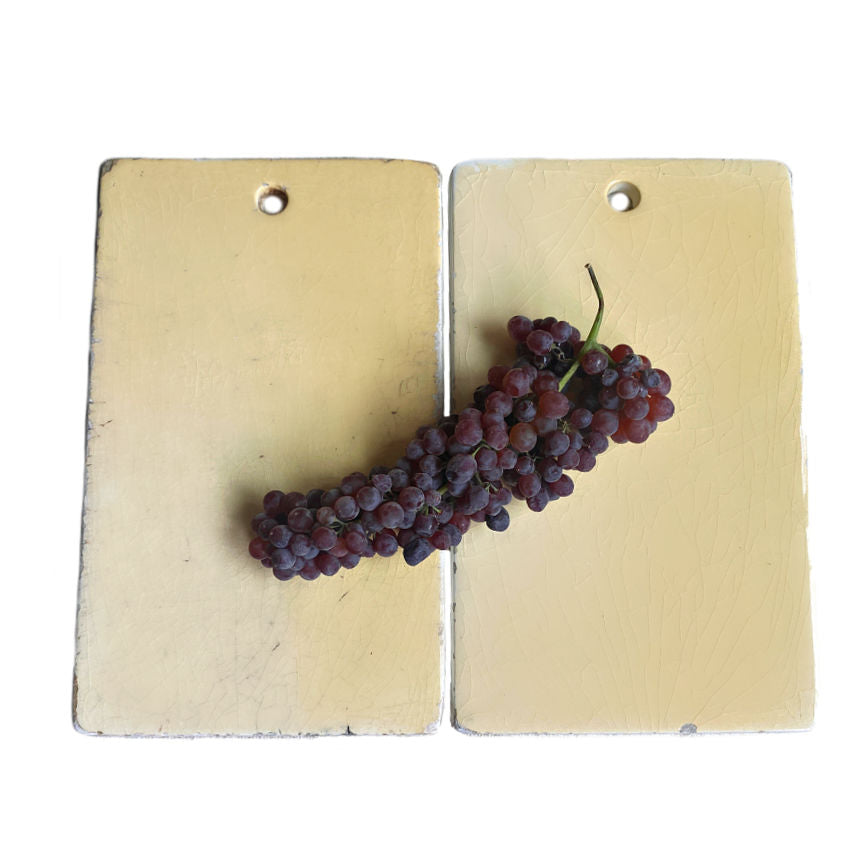 An ironstone cutting board with a yellowish tint and a white reverse side, featuring a cluster of red grapes placed on it.