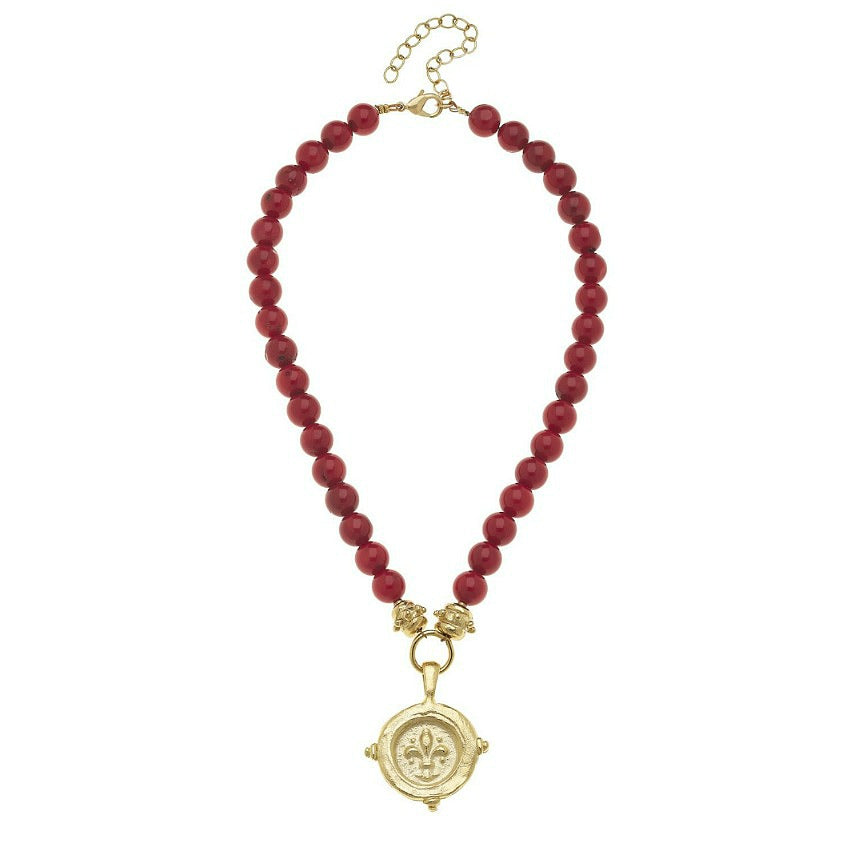 A red semi-precious stone coral necklace with a gold fleur de lis intaglio pendant, featuring a gold-plated chain and a lobster clasp.