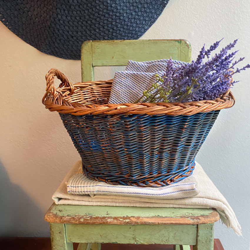 Handwoven Dutch basket in faded Delft blue styled as a decorative centerpiece with dried botanicals and antique textiles